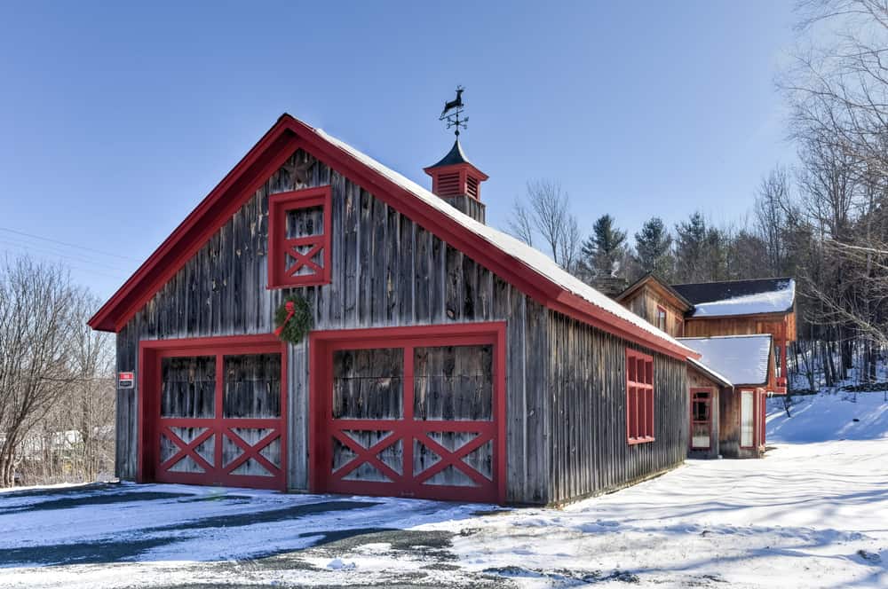 A wooden barn with red trim stands tall in a snowy landscape.