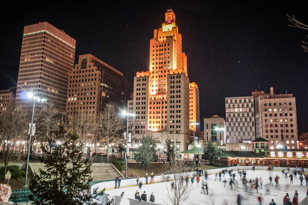 People ice skating at night with a city skyscape behind them.