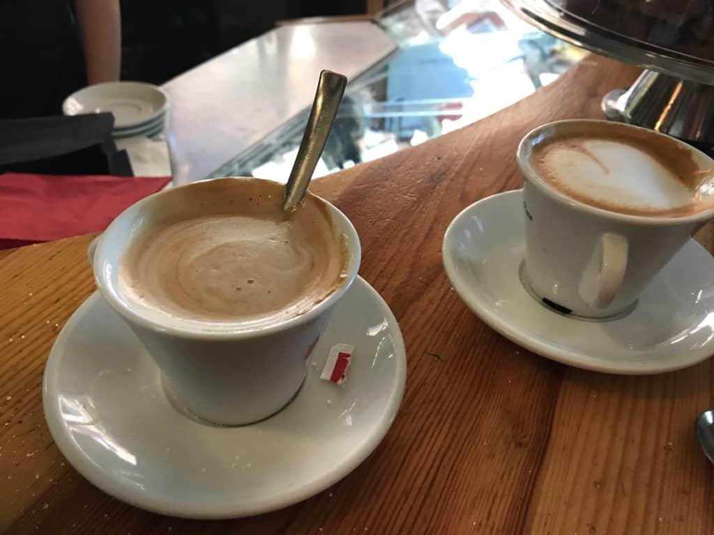 Two white mugs of cappuccinos on a wooden table.