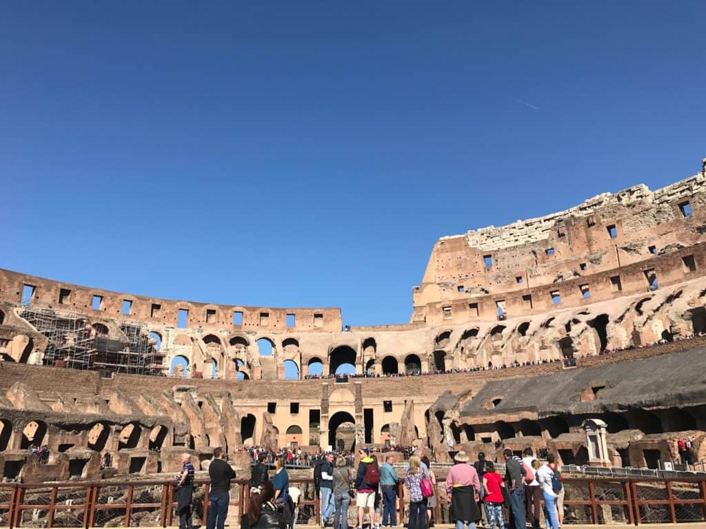 People stand in front of an ancient colosseum. 