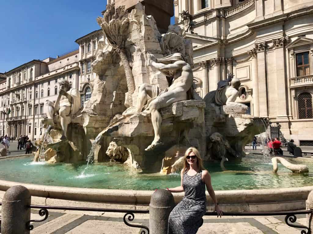 A woman smiles in front of a fountain.