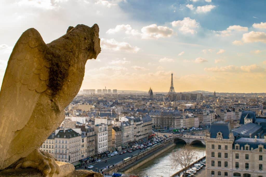 A historic sculpture looks out at the city skyline of Paris. The Eiffel Tower is seen in the background.