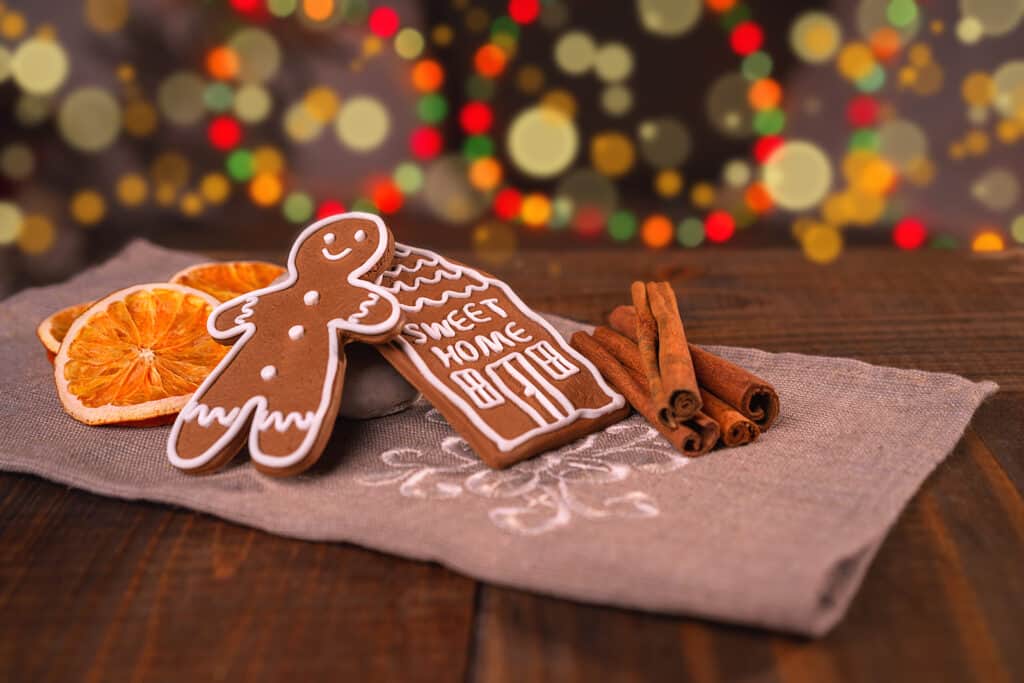 Christmas homemade gingerbread cookies on wooden table, slices of dry orange and colored lights on background. gingerbread man house