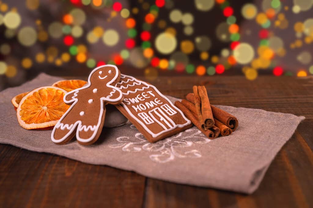 Homemade gingerbread cookies on a wooden table next to slices of dry orange. Colored lights are on in the background.