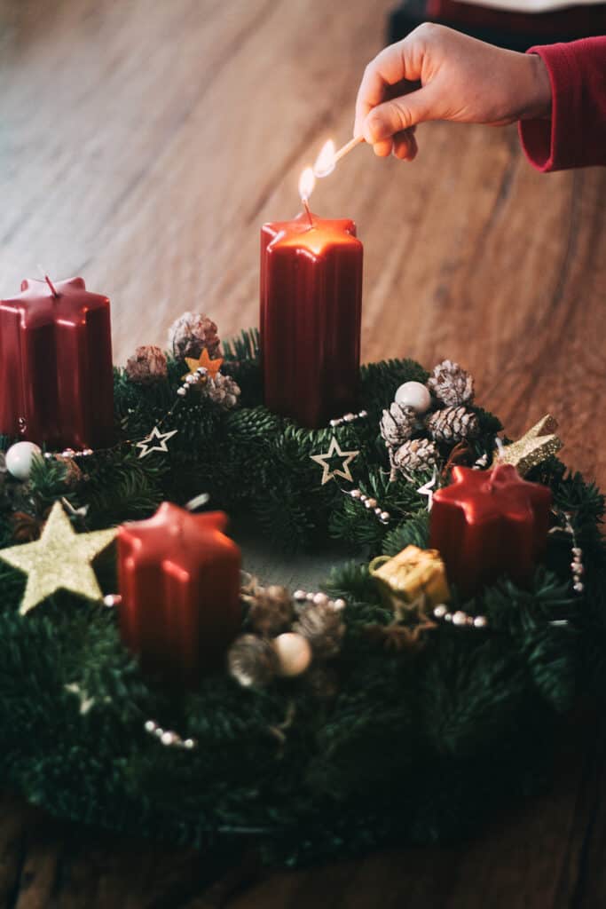 christmas traditions for couples - lighting the first candle on Advent wreath four weeks before Christmas as traditionally in Switzerland. Crop hand lighting the first candle, closeup.