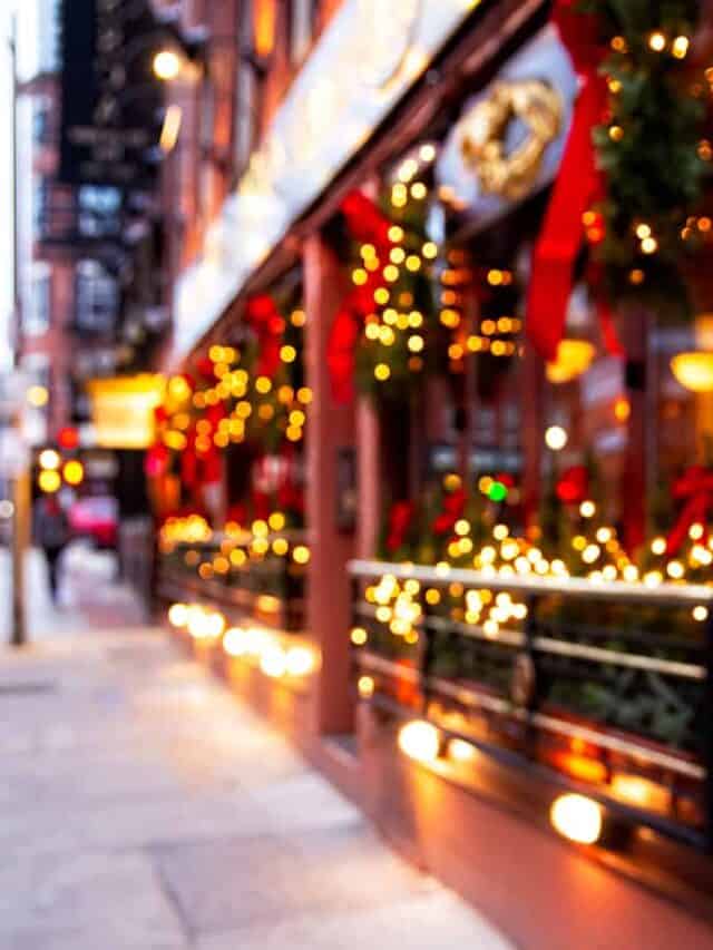 A blurred image of a city street lined with shops that all have holiday decor up.