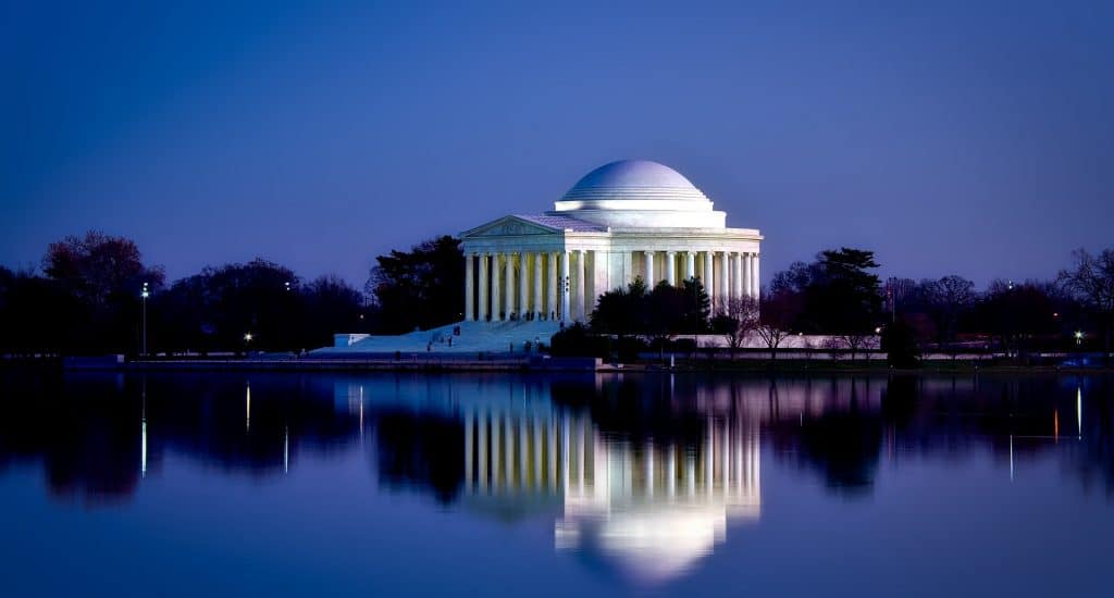 White memorial building reflecting on a lake under a purple sky.