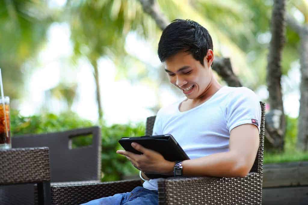 A man sits looking at an ipad outdoors.