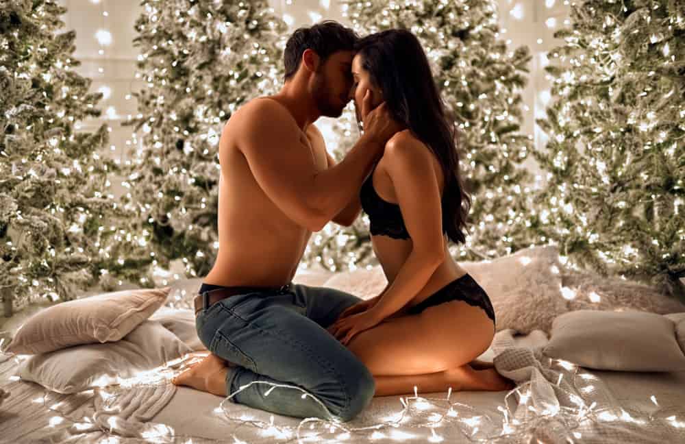 A couple intimately kisses on a Christmas date surrounded by lighted trees