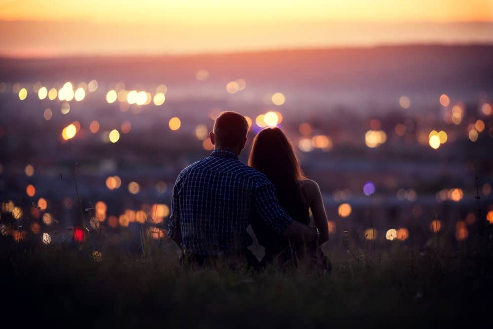 A couple sits while looking out at the city at sunset.