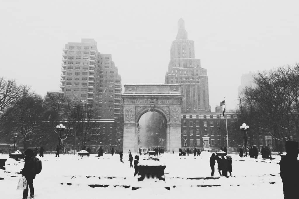 People walking around a snowy plaza with city buildings behind.