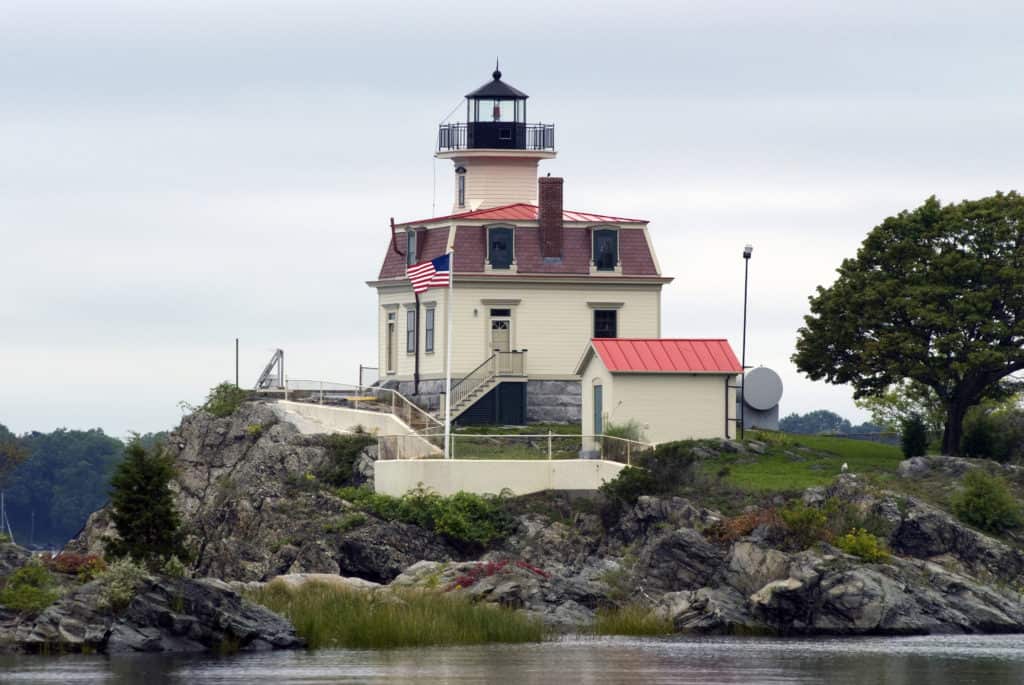 A tall white lighthouse stands on an island under a blue sky.