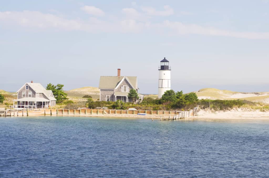 A white lighthouse stands next to a grey building on the coast.