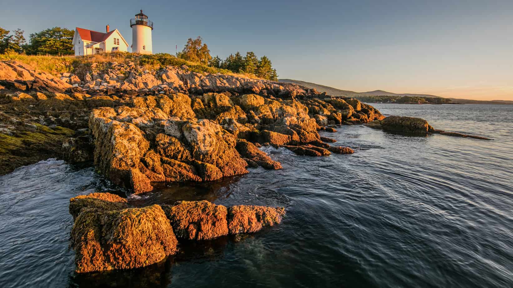 A lighthouse stands on an island by the coast.