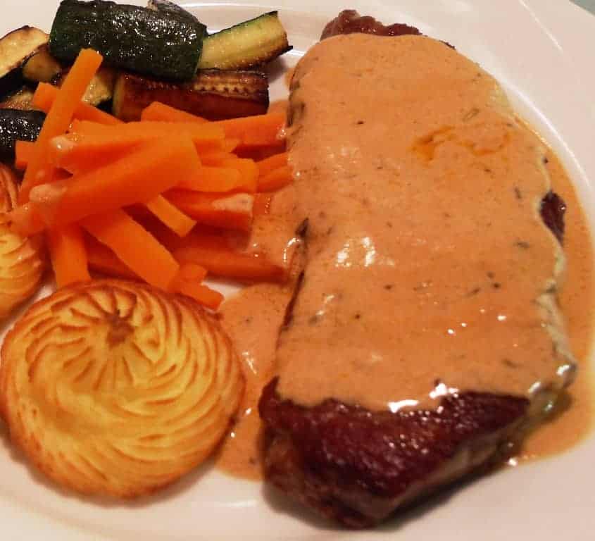 A plate of food, with Steak and Sauce. Vegetables are next to the steak.