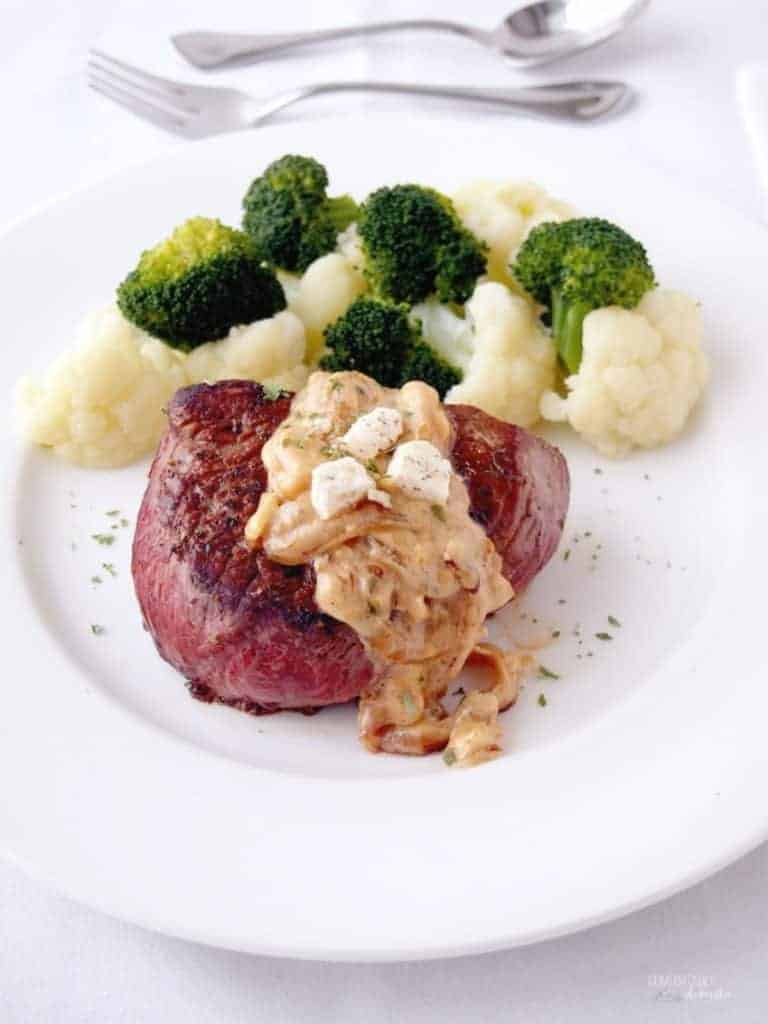 Steak with onion sauce next to broccoli and cauliflower.