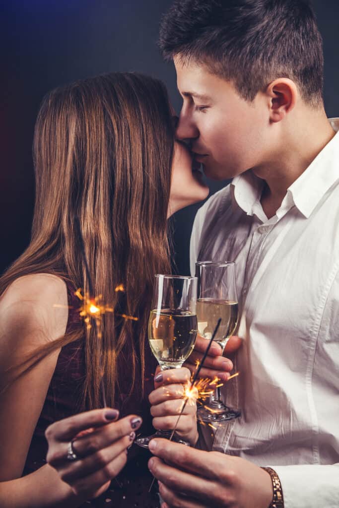 A couple kisses while holding champagne flutes.