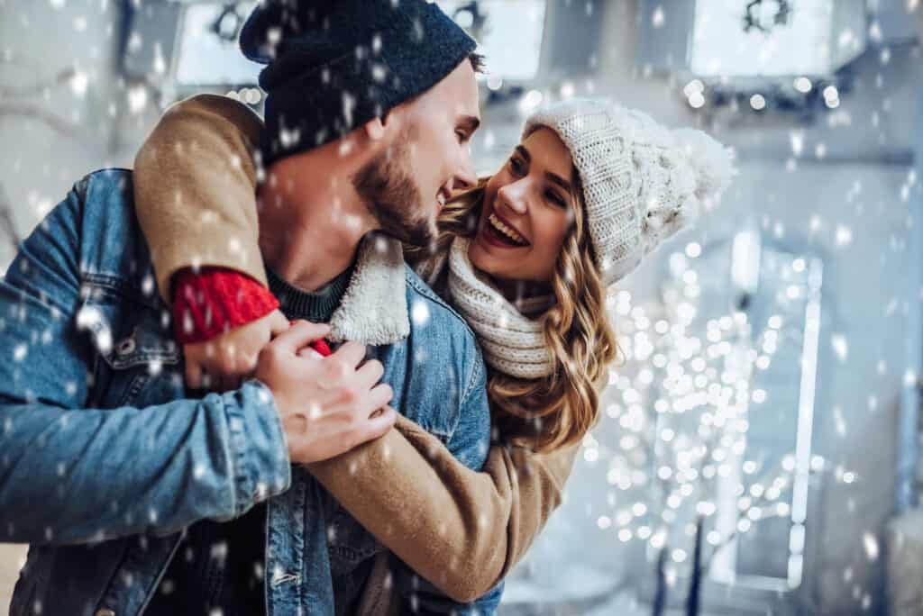 A couple embraces and smiles at each other on an outdoor Christmas date