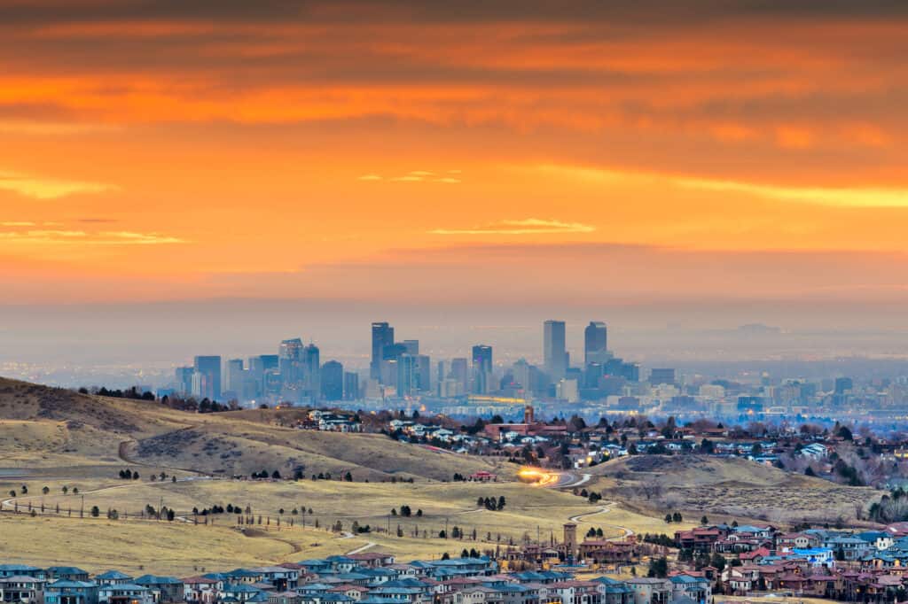 A city skyline with green space in the foreground. The sky is orange.