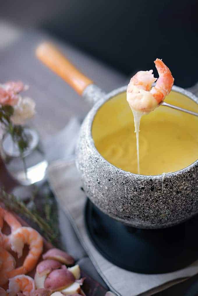 A skewer dips shrimp into cheese.