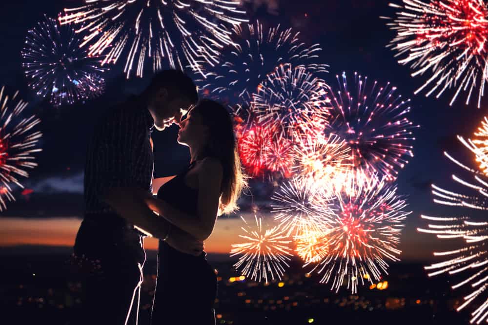 Fireworks go off behind a couple as they embrace.