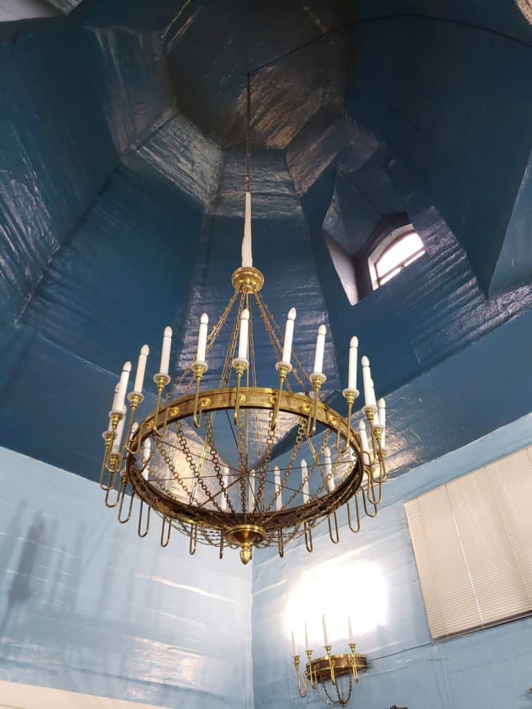 Gold chandelier with candles hanging from a blue ceiling.