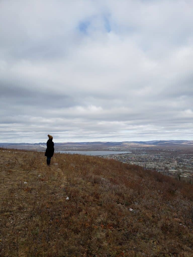 A person in a hat looks out from a mountain at the town below.