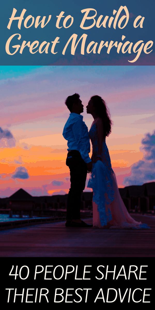 A couple stands holding hands with the sun setting behind them.