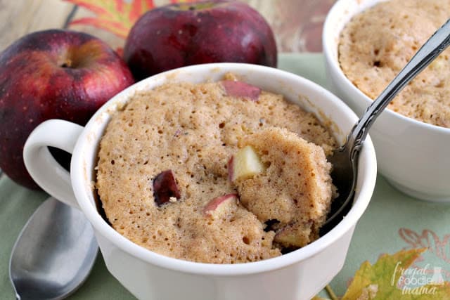 A spoon pulls a mug cake with apples out of a cup.