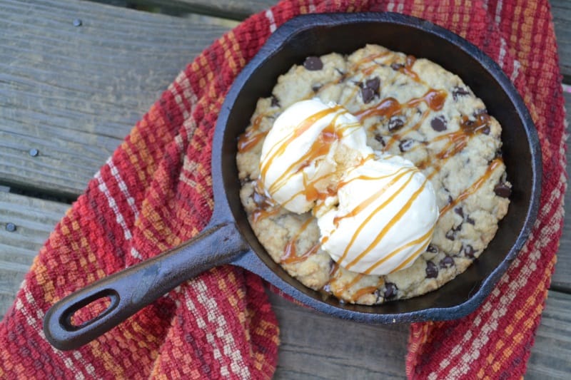 A skillet has cookie dough with ice cream and caramel on top.