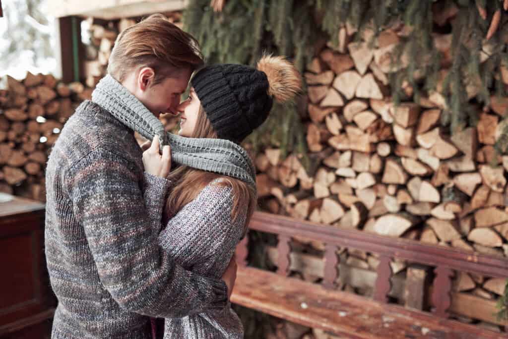 A hipster couple hugs each other outdoors while wearing winter sweathers.