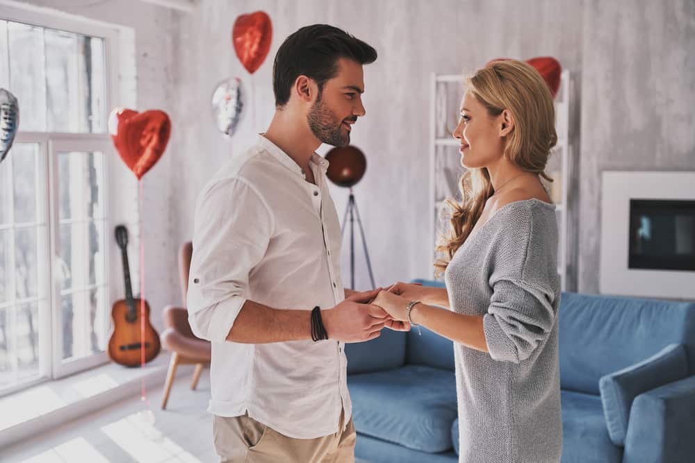 romantic couple holding hands in living room with heart balloons in background - valentines date night