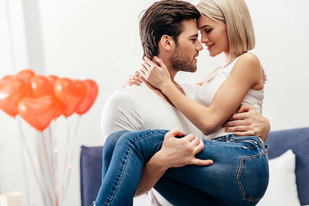 A man holds a woman in his arms while gazing into her eyes.