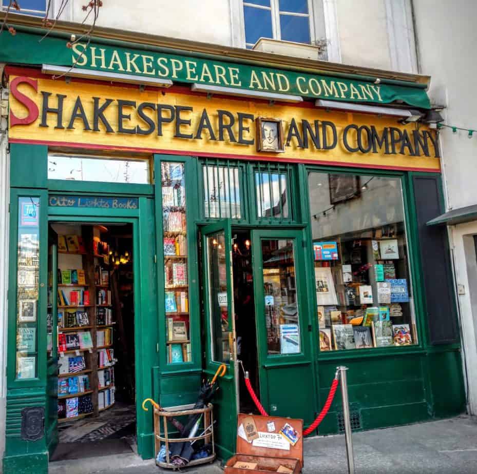 A green storefront that says \"Shakespeare and Company.\" Inside it\'s filled with books.