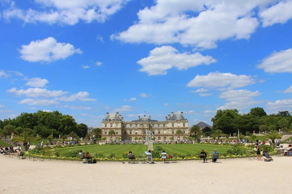 People relax in a garden with a big building in the background.