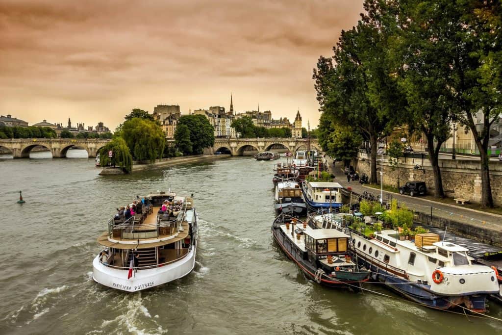 People are on a cruise that is going along the river under a pink sky.