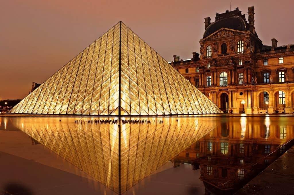 The Louvre is illuminated at night under a purple sky.