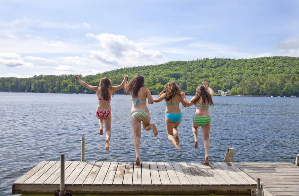 A group of friends jump into the lake from a wooden pier.