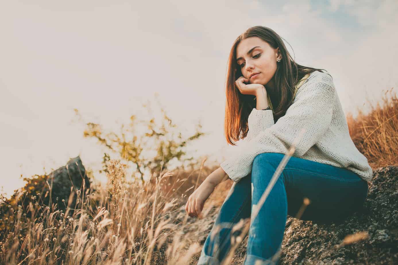 A girl sits alone outdoors while wearing a sweater.