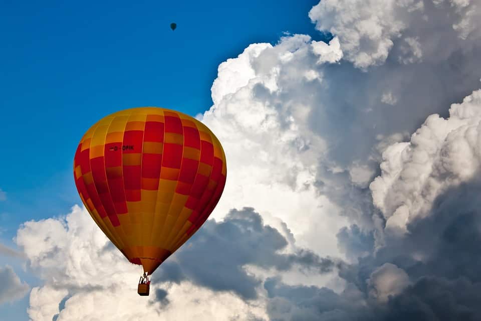 A hot air balloon floats in the sky with bright white clouds.