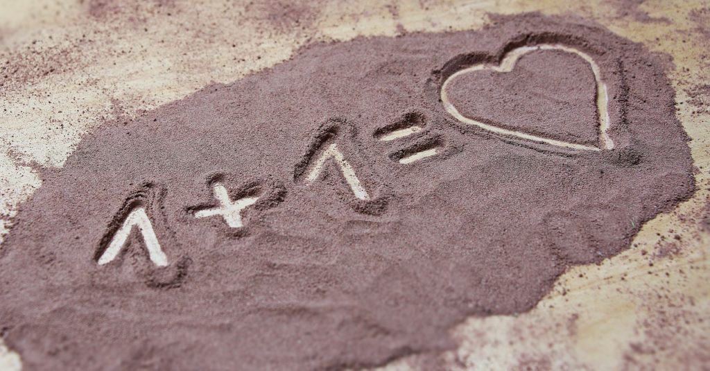 A sweet message written in the sand that says 1 + 1 = heart.