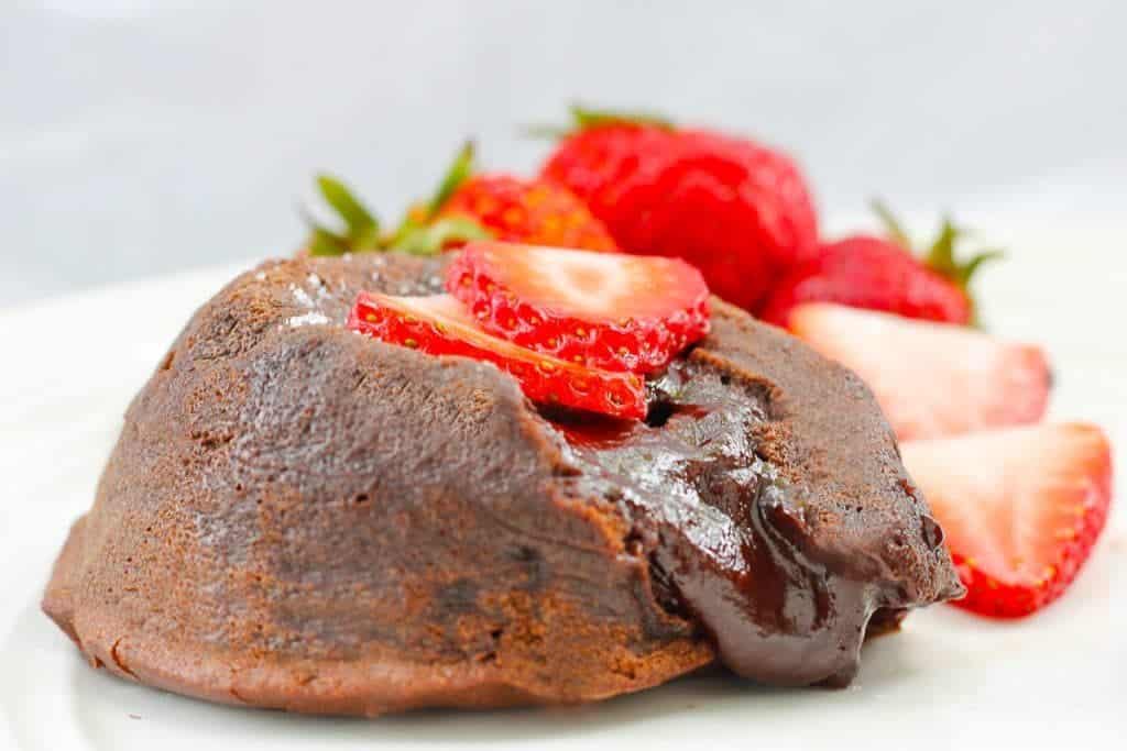 A close up of a molten lava cake oozing chocolate with strawberries on top.