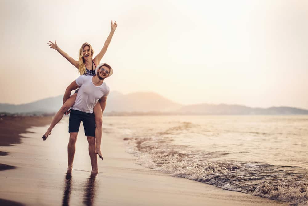 A couple is on piggyback near the beach having a good time.