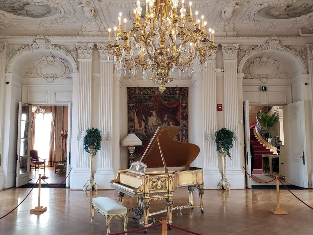 A big chandelier hangs down over a gold piano.