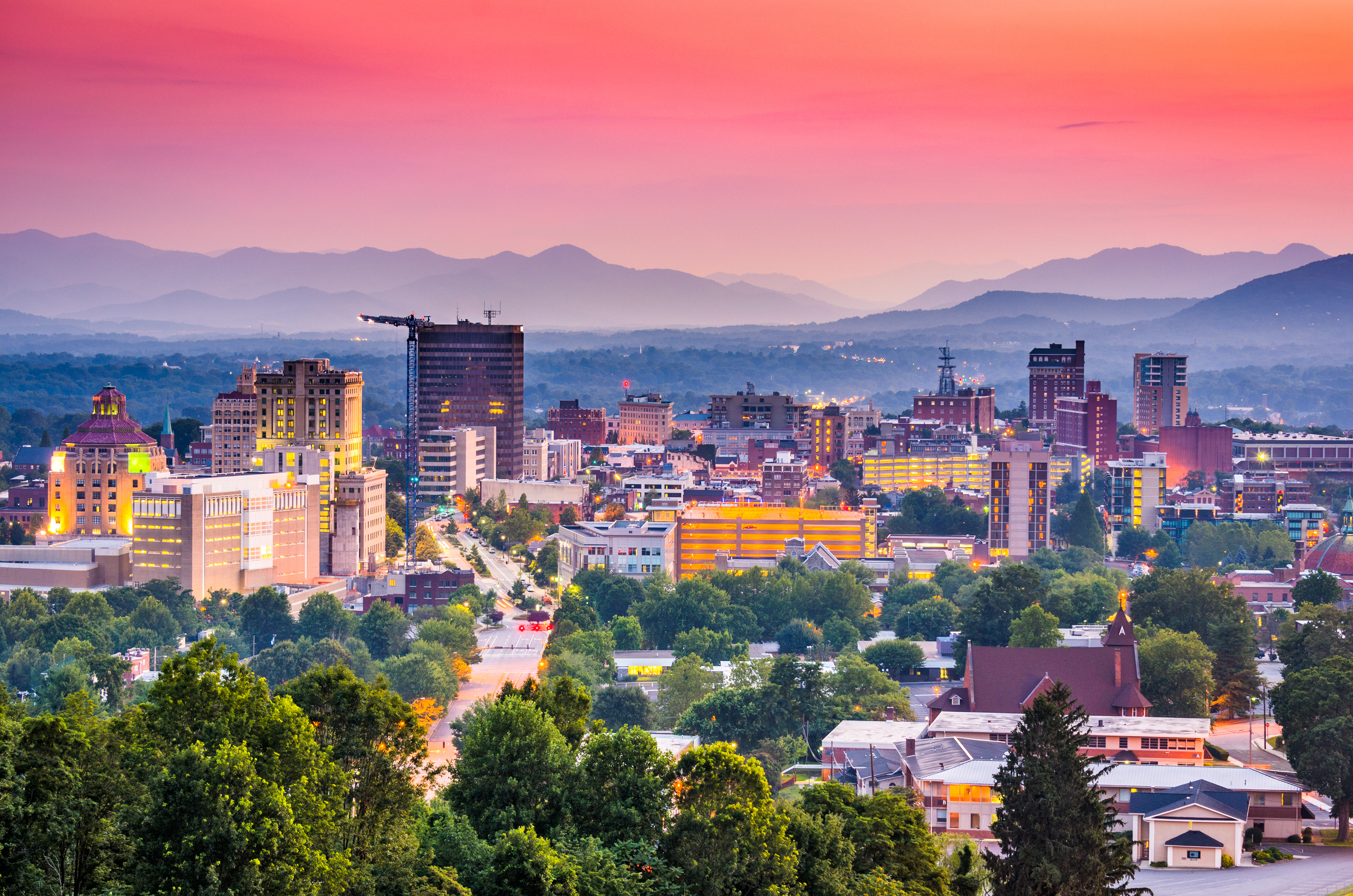 City skyline view with lots of greenery. The sky is pink above it.