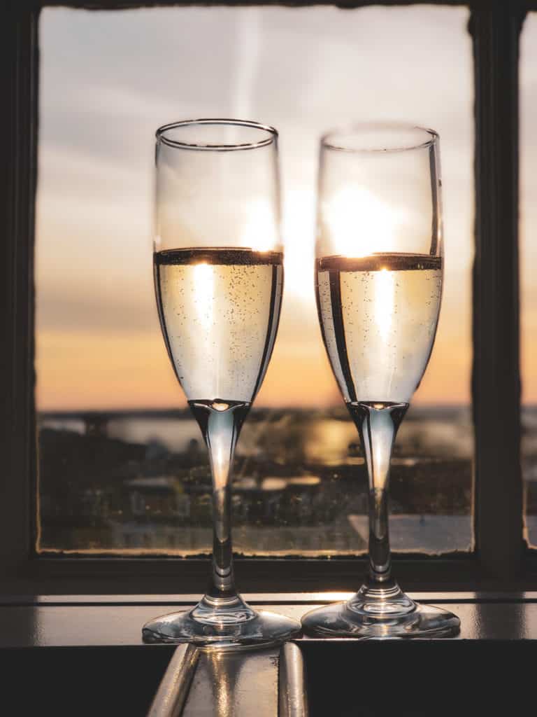 Two glasses of champagne in a window with the sunset behind.