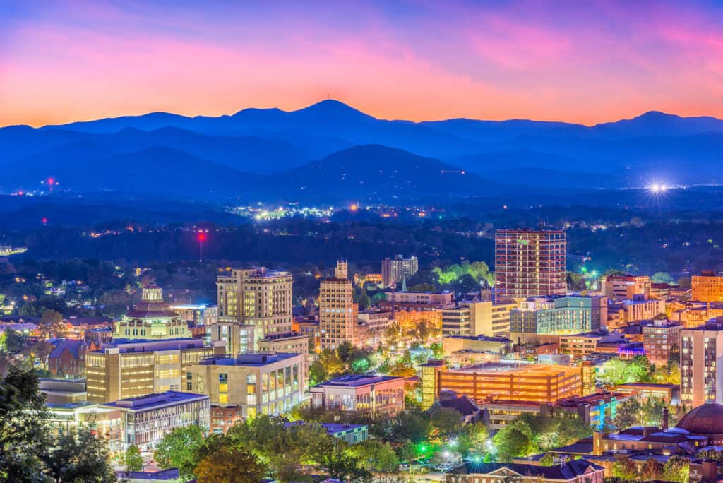 View of a city skyline with mountains behind under a pink and purple sky.