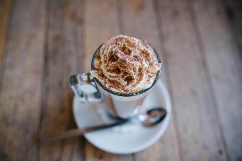 A cup of hot cocoa sits on a table with whipped cream and cocoa powder.