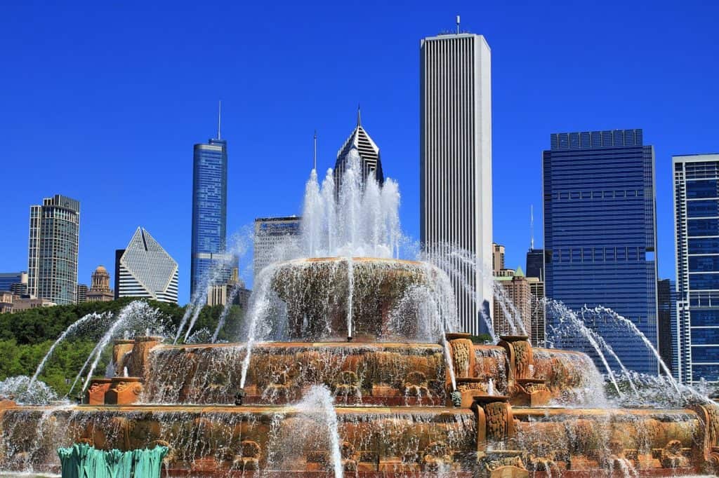 A view of a fountain on a sunny day with a city skyline behind.