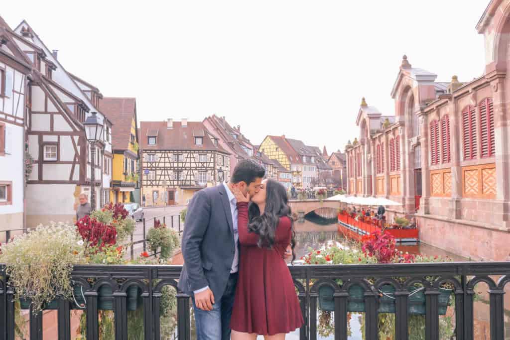 luxury honeymoon Europe - Alsace France couple kissing in front of a picturesque village